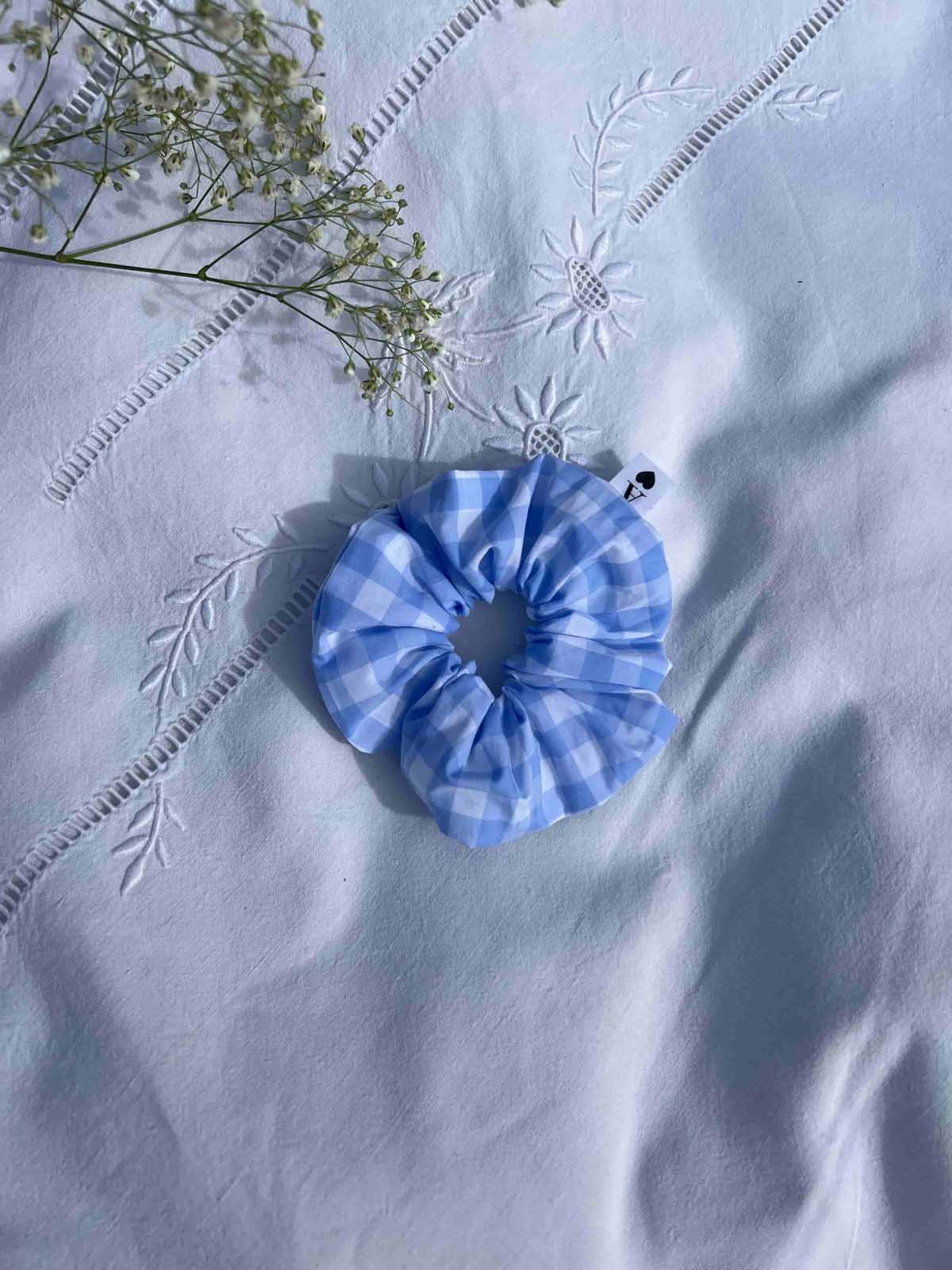 chouchou en popeline vichy bleu posé sur un drap