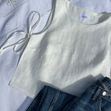 haut douceur en lin blanc noué, posé sur un draps en extérieur avec un jean