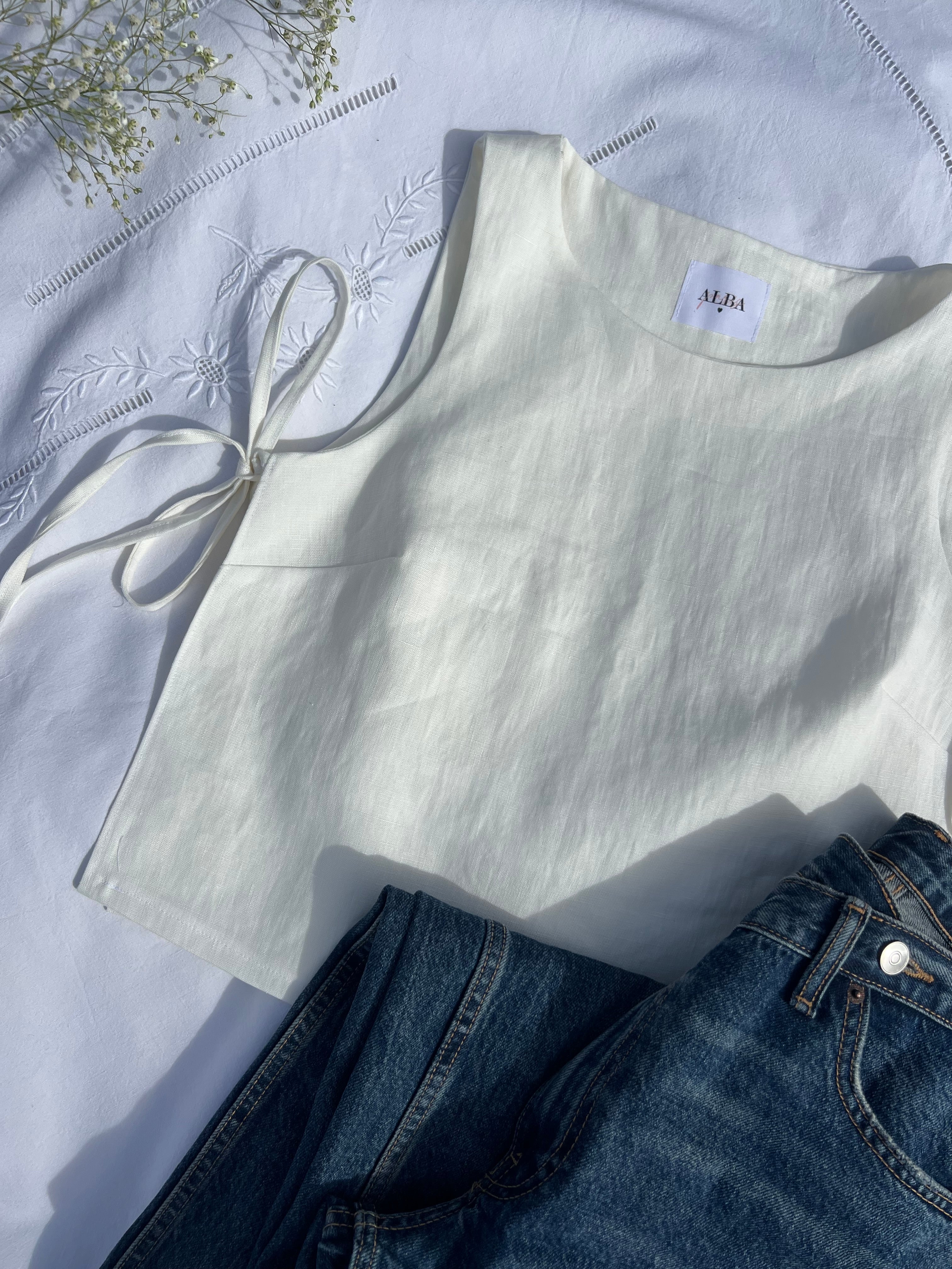 haut douceur en lin blanc noué, posé sur un draps en extérieur avec un jean