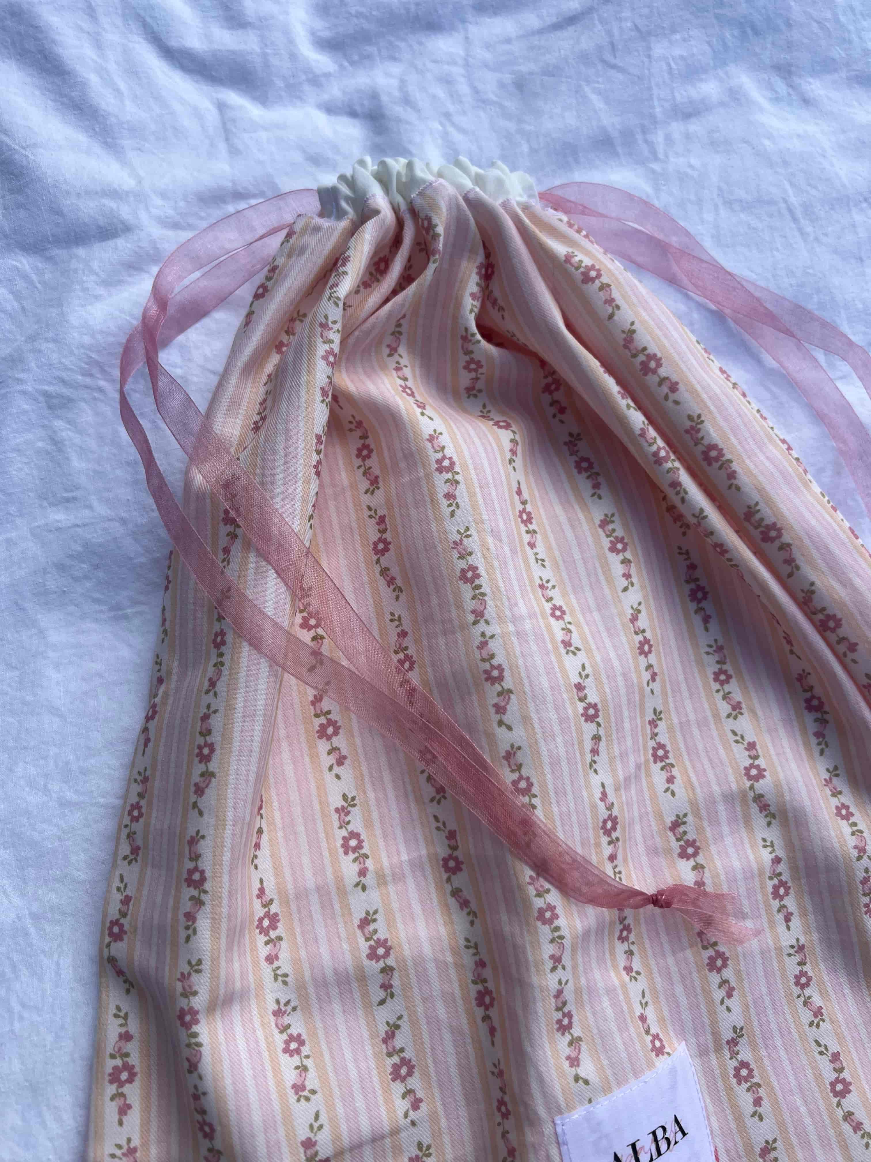 zoom détails sac à chaussures / rangement, rayures fleurs et popeline blanc, fermé et posé sur un drap