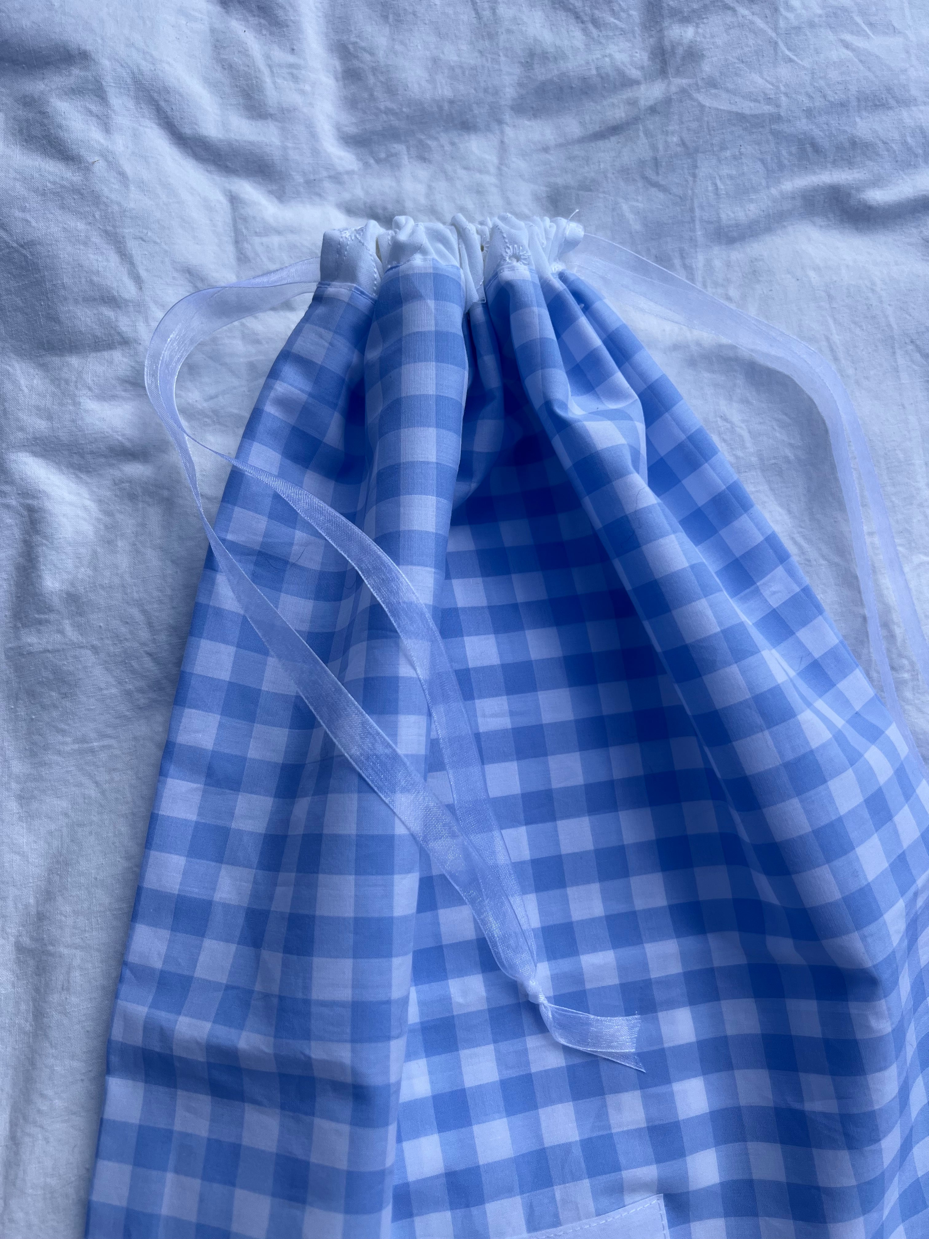zoom détails sac à chaussures / rangement, broderie anglaise et popeline vichy bleu, fermé et posé sur un drap