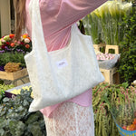 sac mael en dentelle blanche porté à l'épaule en extérieur fleurs, avec chemise rose et jupe en dentelle