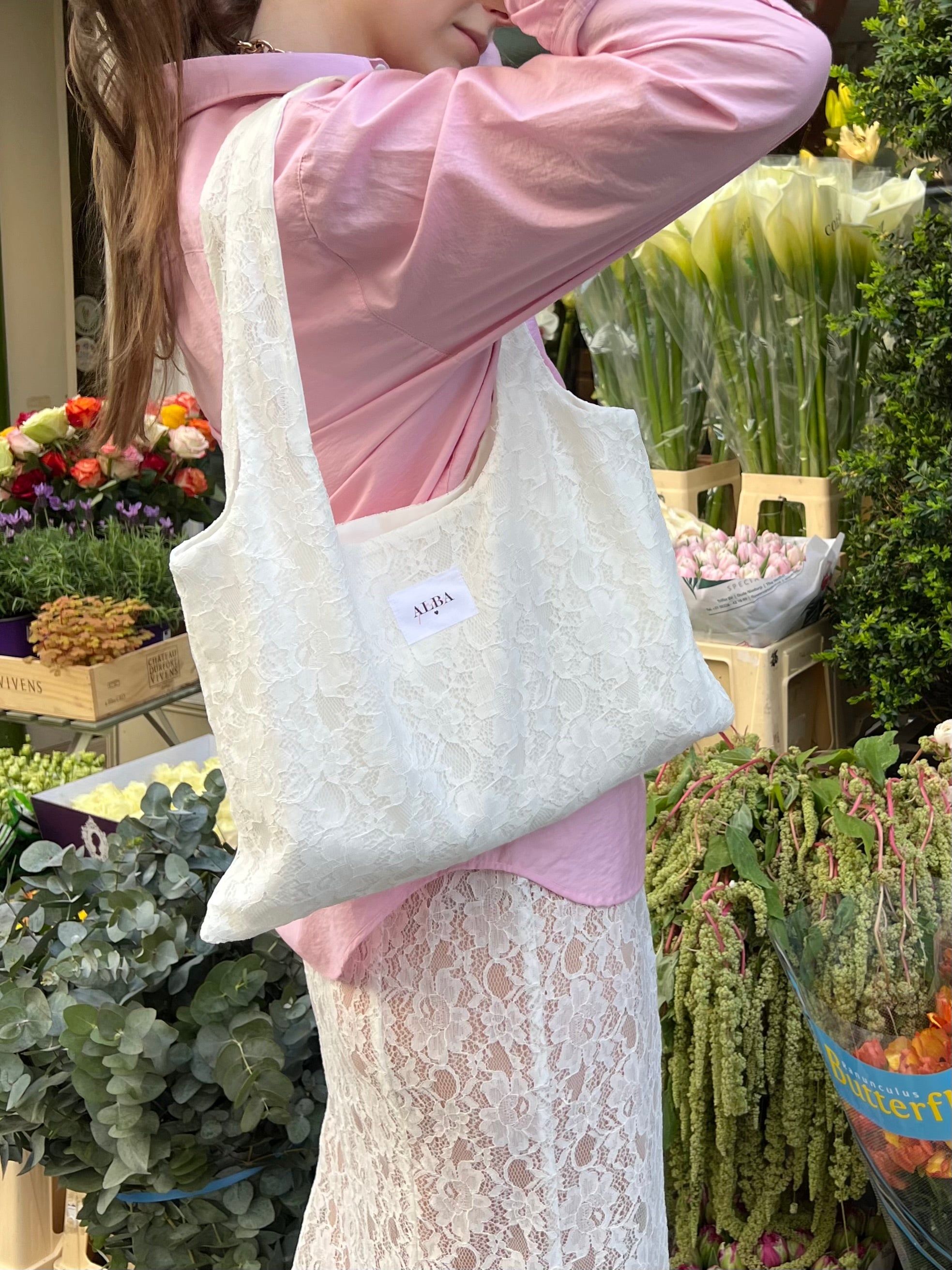 sac mael en dentelle blanche porté à l'épaule en extérieur fleurs, avec chemise rose et jupe en dentelle