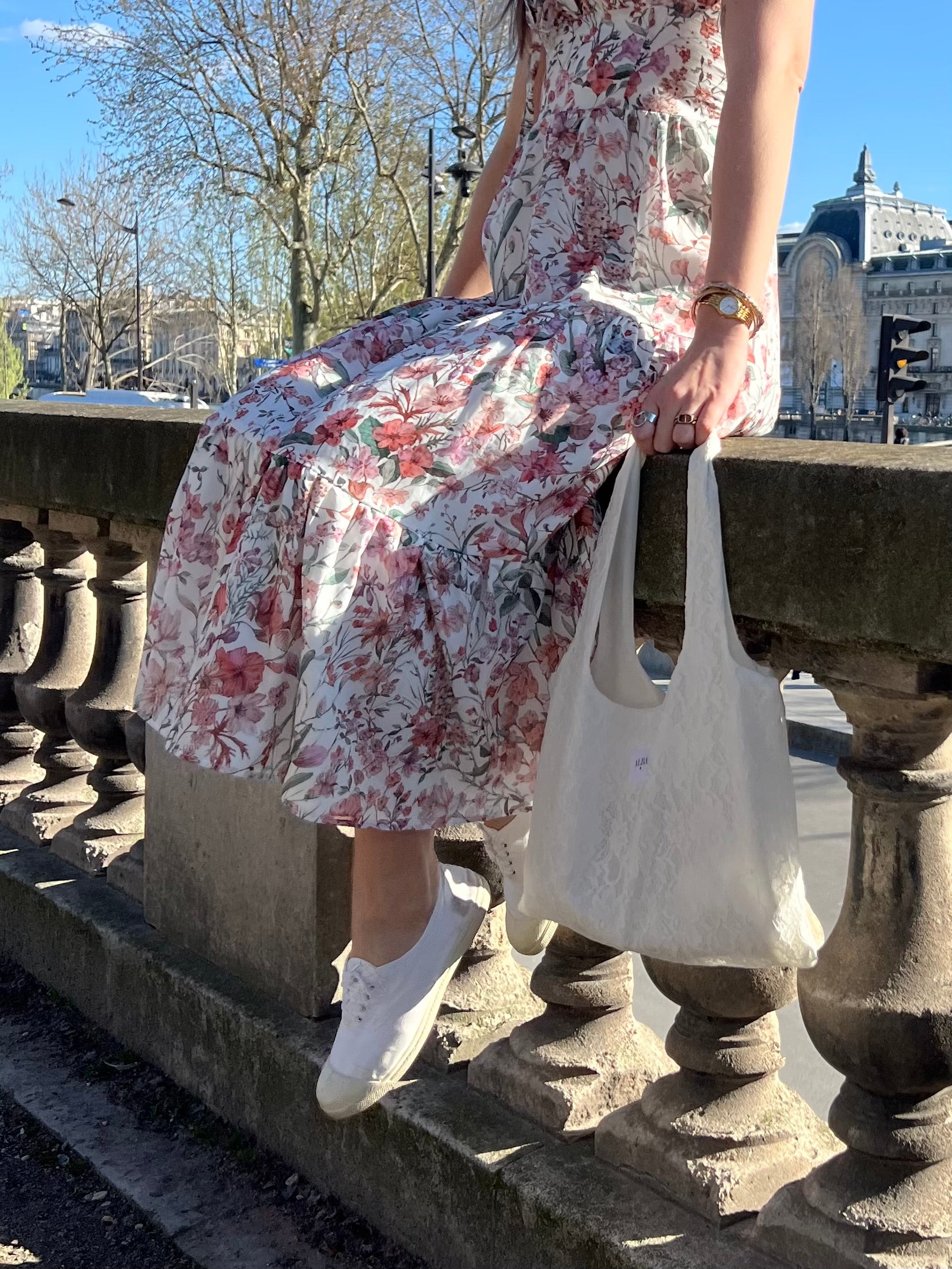 sac mael en dentelle blanche porté à la main avec robe simone à fleurs spring assis en extérieur 