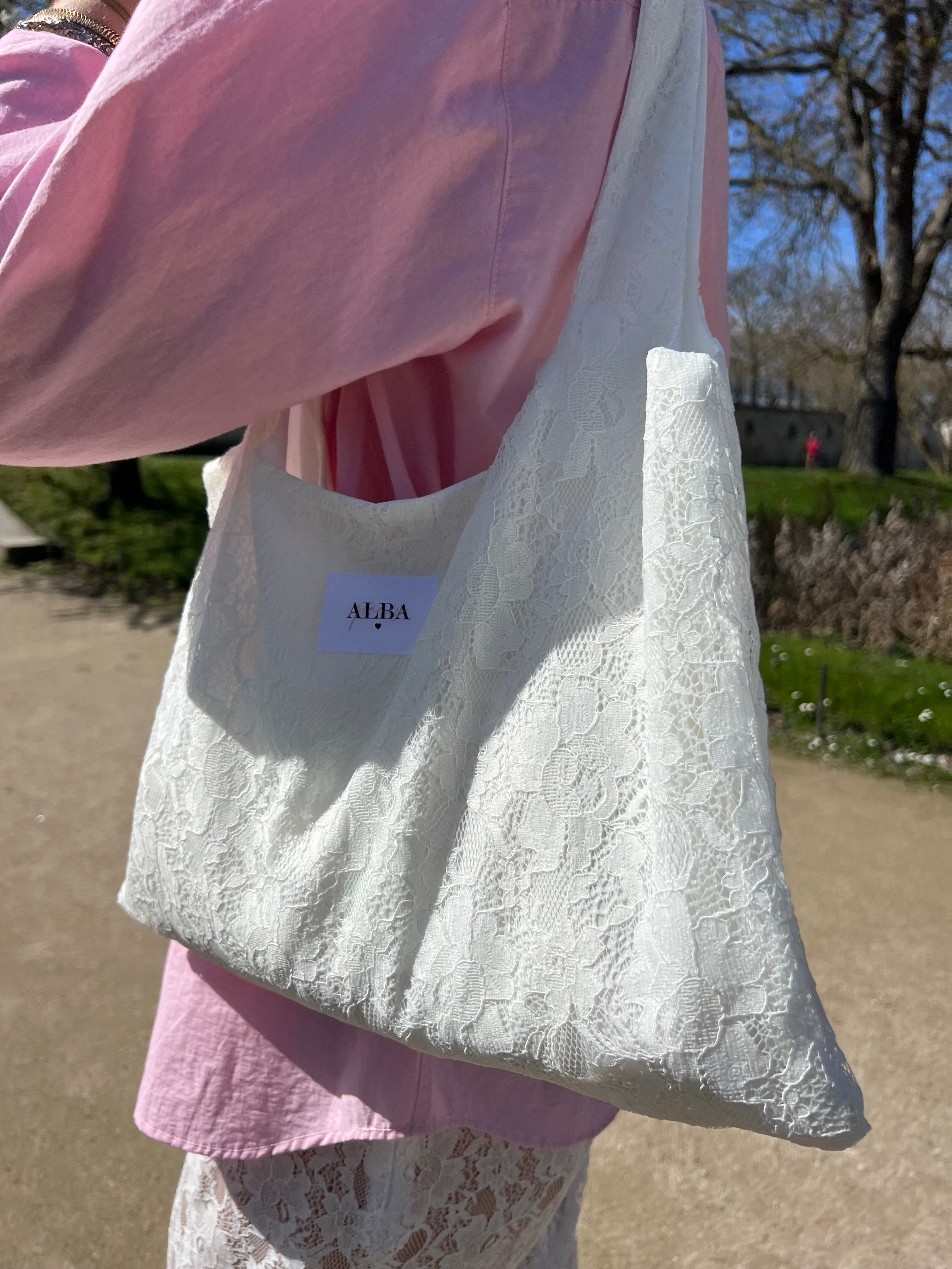 sac mael en dentelle blanche porté à l'épaule en extérieur avec jupe en dentelle et chemise rose zoom