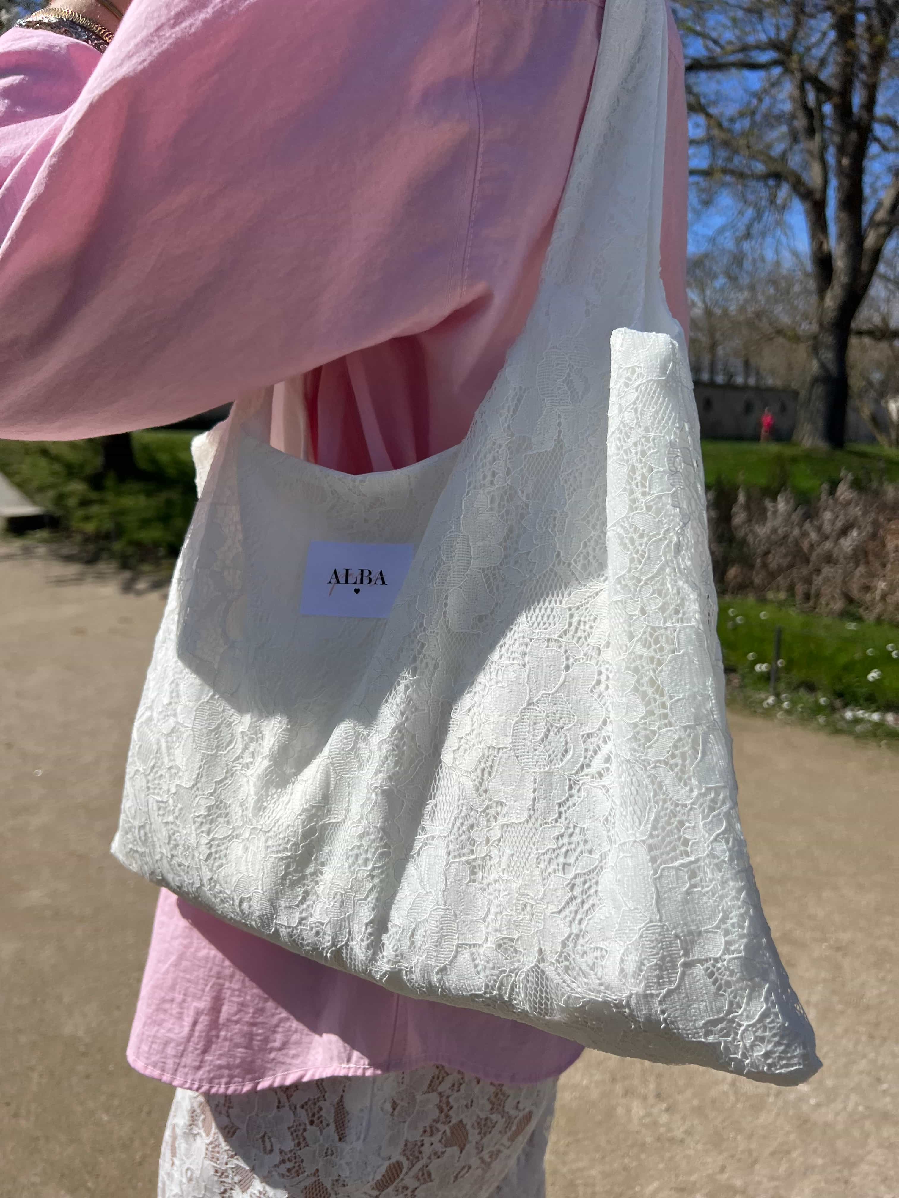 sac mael en dentelle blanche porté à l'épaule en extérieur avec jupe en dentelle et chemise rose zoom