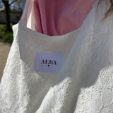 sac mael en dentelle blanche porté à l'épaule en extérieur avec chemise rose zoom