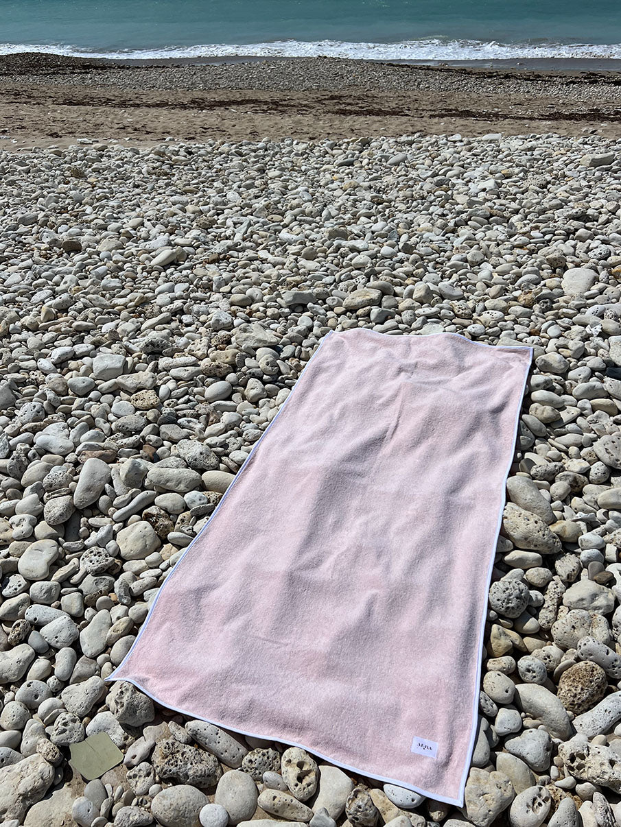serviette de plage rose et blanc ALBA posée sur galets